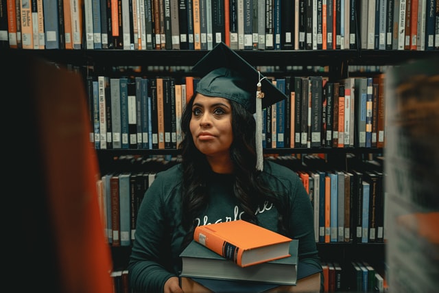 An apprehensive student holds a stack of textbooks in a library.